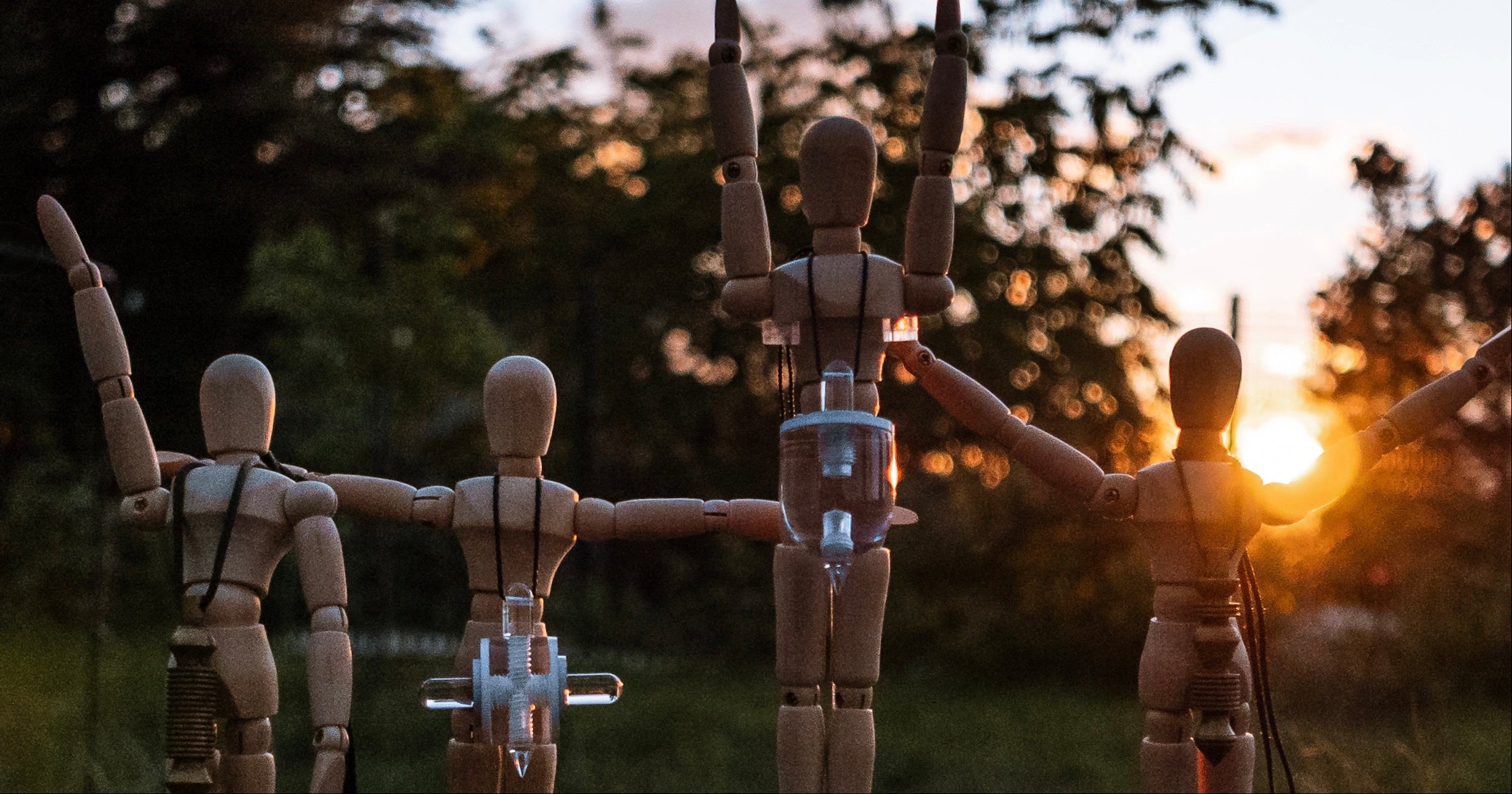 Wooden mannequins in a circle with a sunset in the background